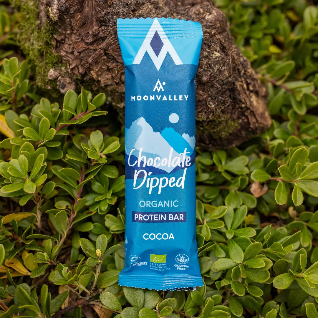 Moonvalley økologisk proteinbar med kakao og sjokoladetrekk, fotografert i naturlige omgivelser.