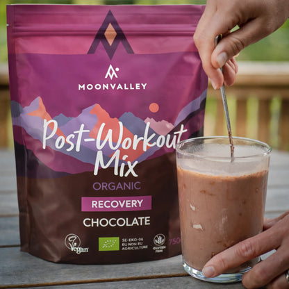 Et glass med ferdigblandet sjokoladedrikk fra Moonvalley Post-Workout Mix røres med en skje.